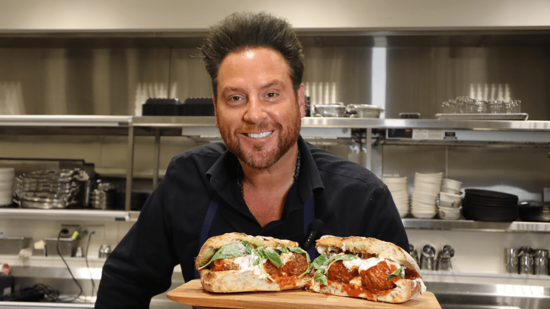 Celebrity Chef holding out a sandwich in a kitchen